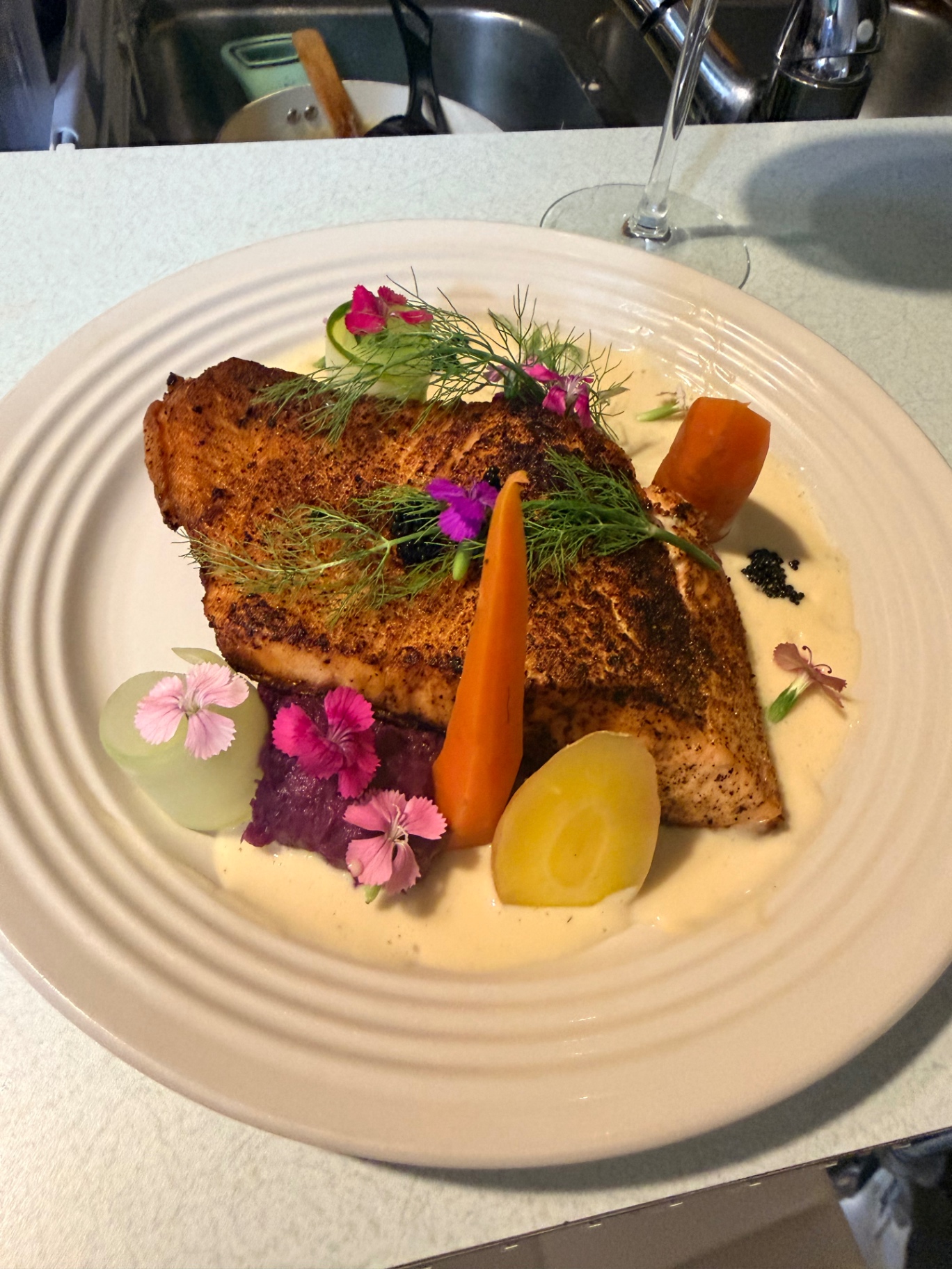 Salmon plated with creamy sauce, vegetables, and edible flowers